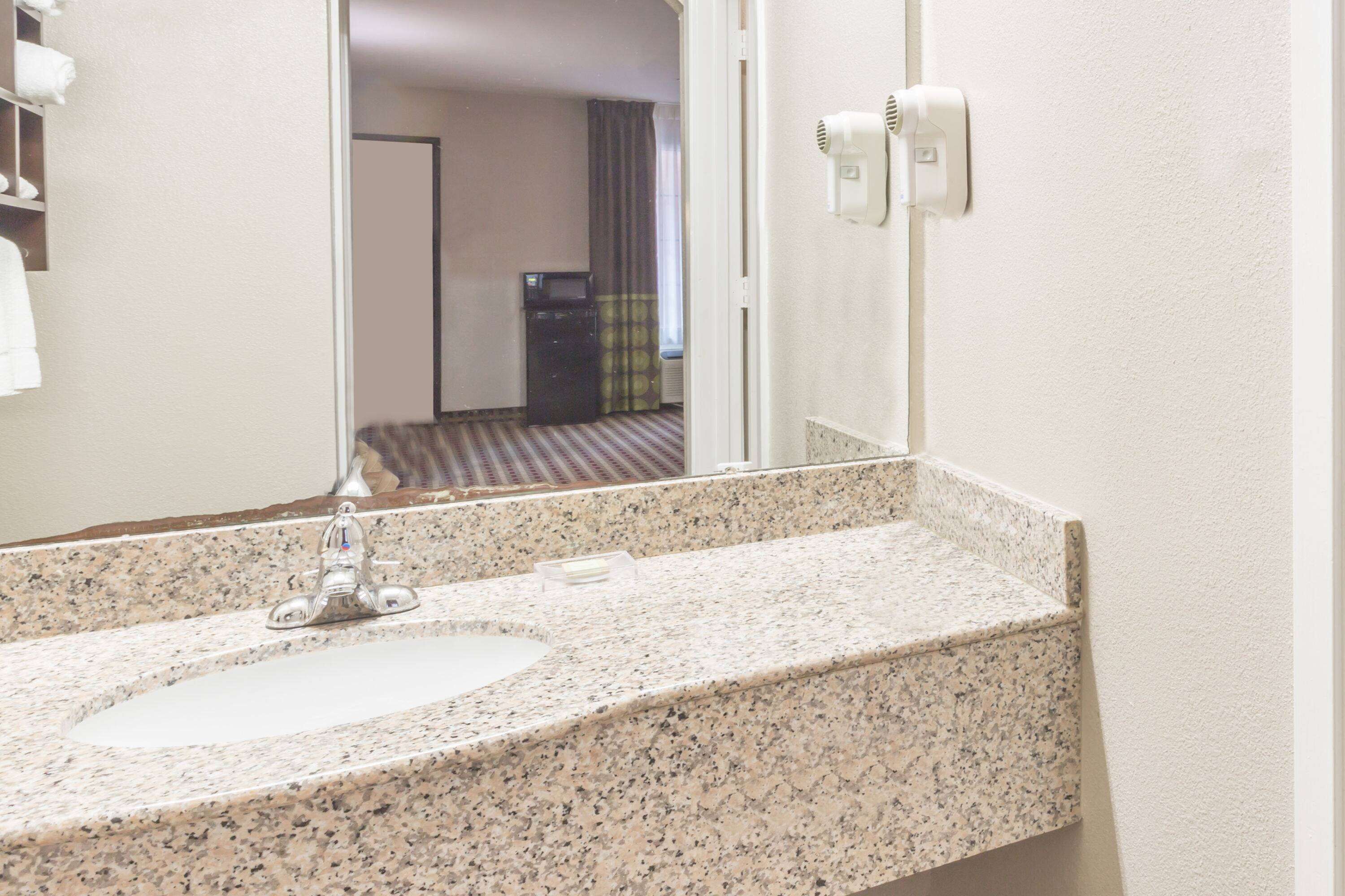 A bathroom with a granite countertop sink, a mirror, and a towel rack.