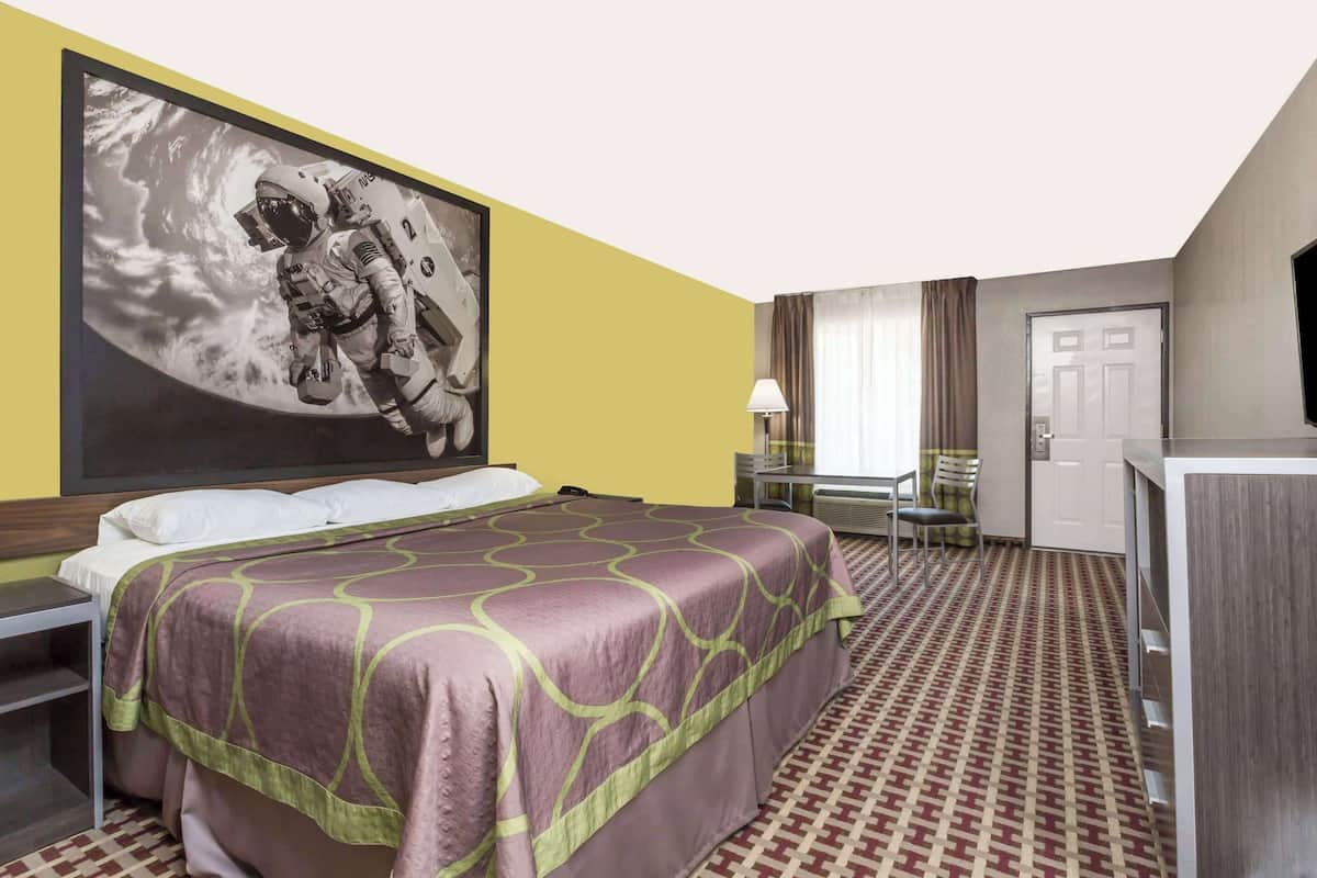 A hotel room with a bed, a desk, a chair, a television, and a large astronaut picture on the wall.