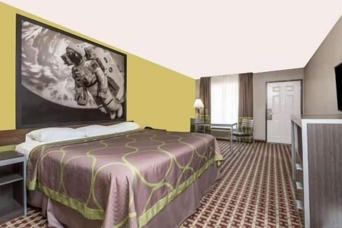 A hotel room with a bed, a desk, a chair, a television, and a door.