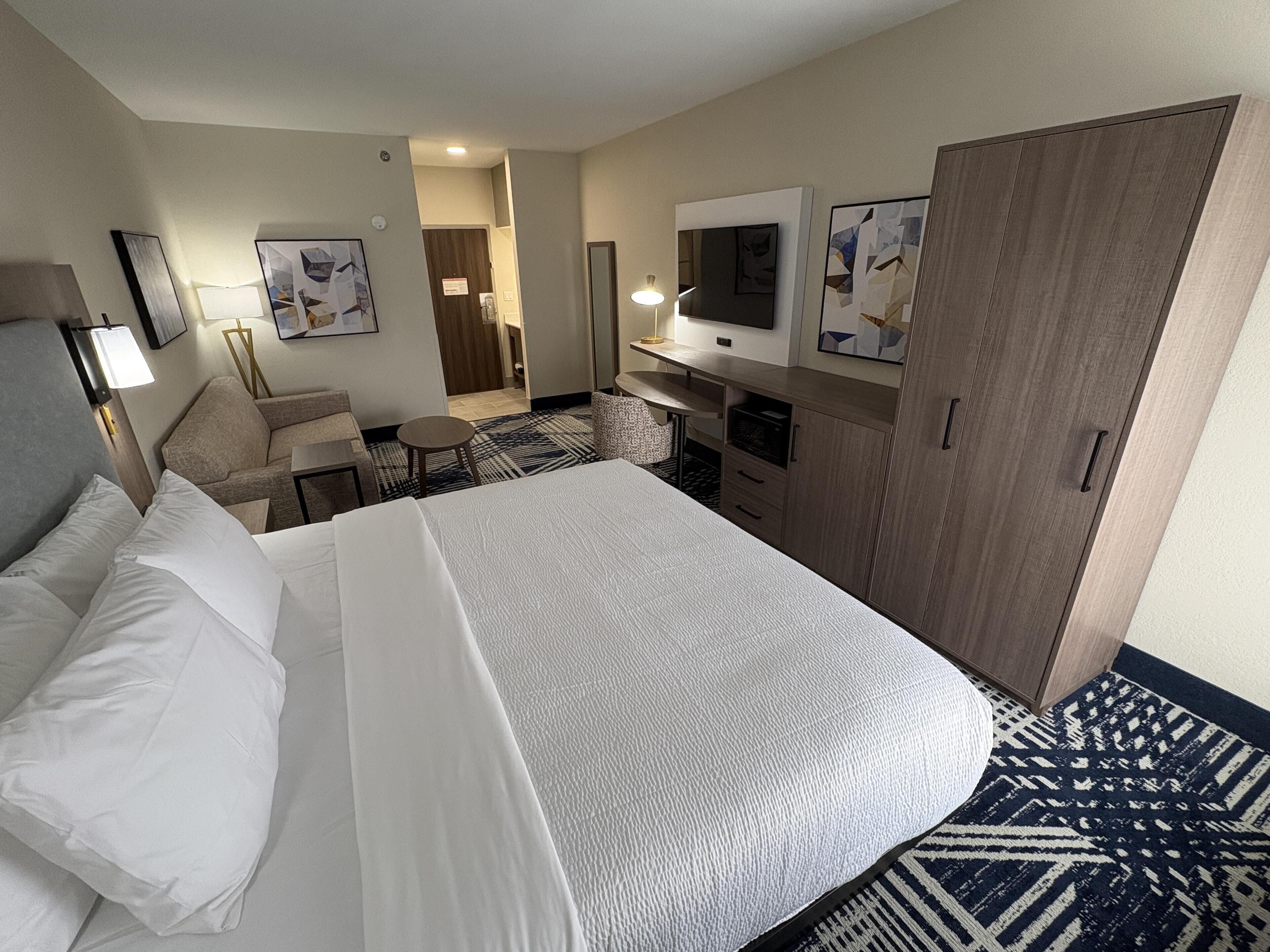 A hotel room with a bed, a desk, a chair, a television, and a wardrobe.
