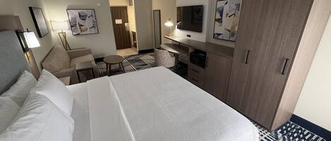 Una habitación de hotel con cama, escritorio, silla, televisor y armario.