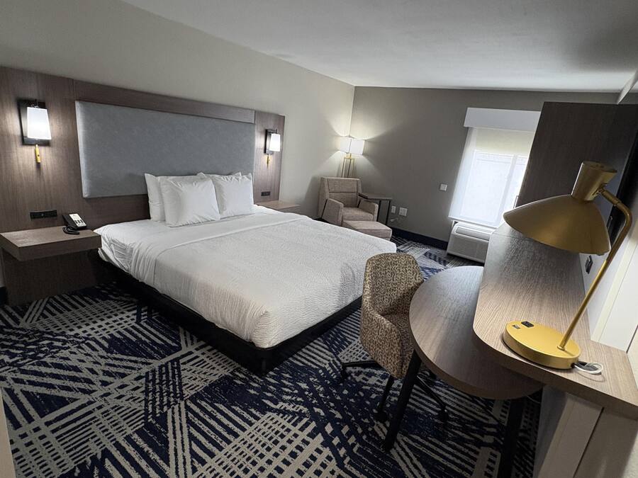 A hotel room with a large bed, bedside tables, a chair, a desk, and a lamp.