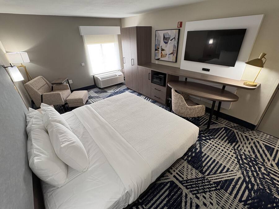 A hotel room with a bed, a desk, a chair, a TV, and a window.
