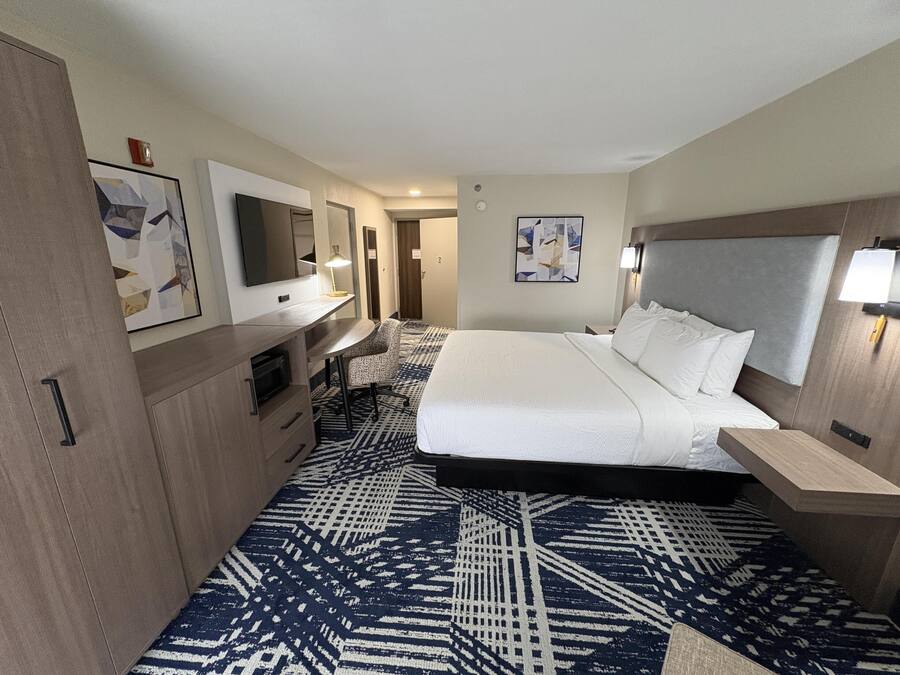 A hotel room with a bed, desk, chair, and a TV.