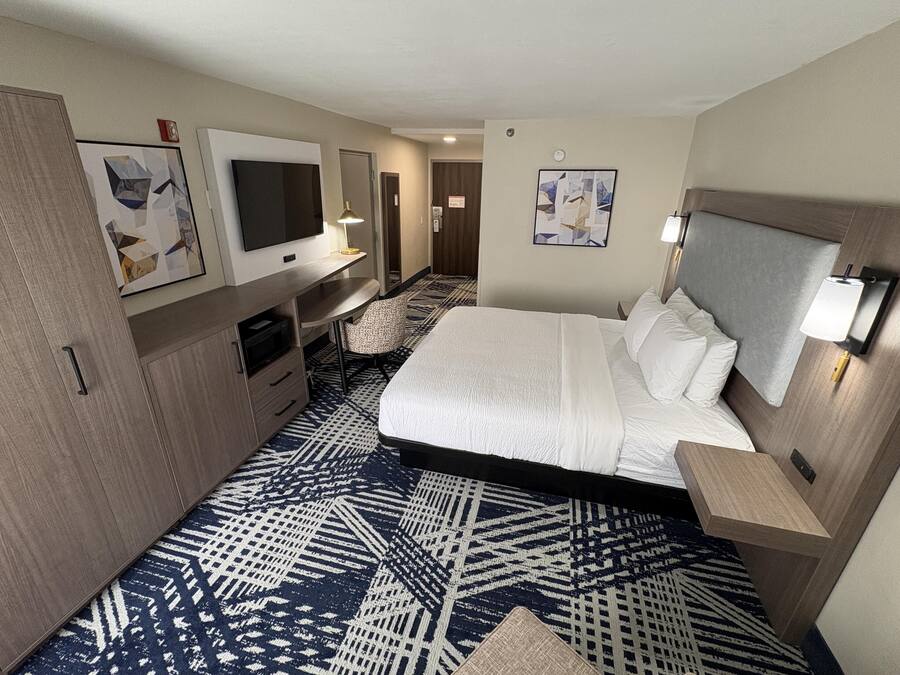Una habitación de hotel con cama, escritorio, televisión y obras de arte en las paredes.