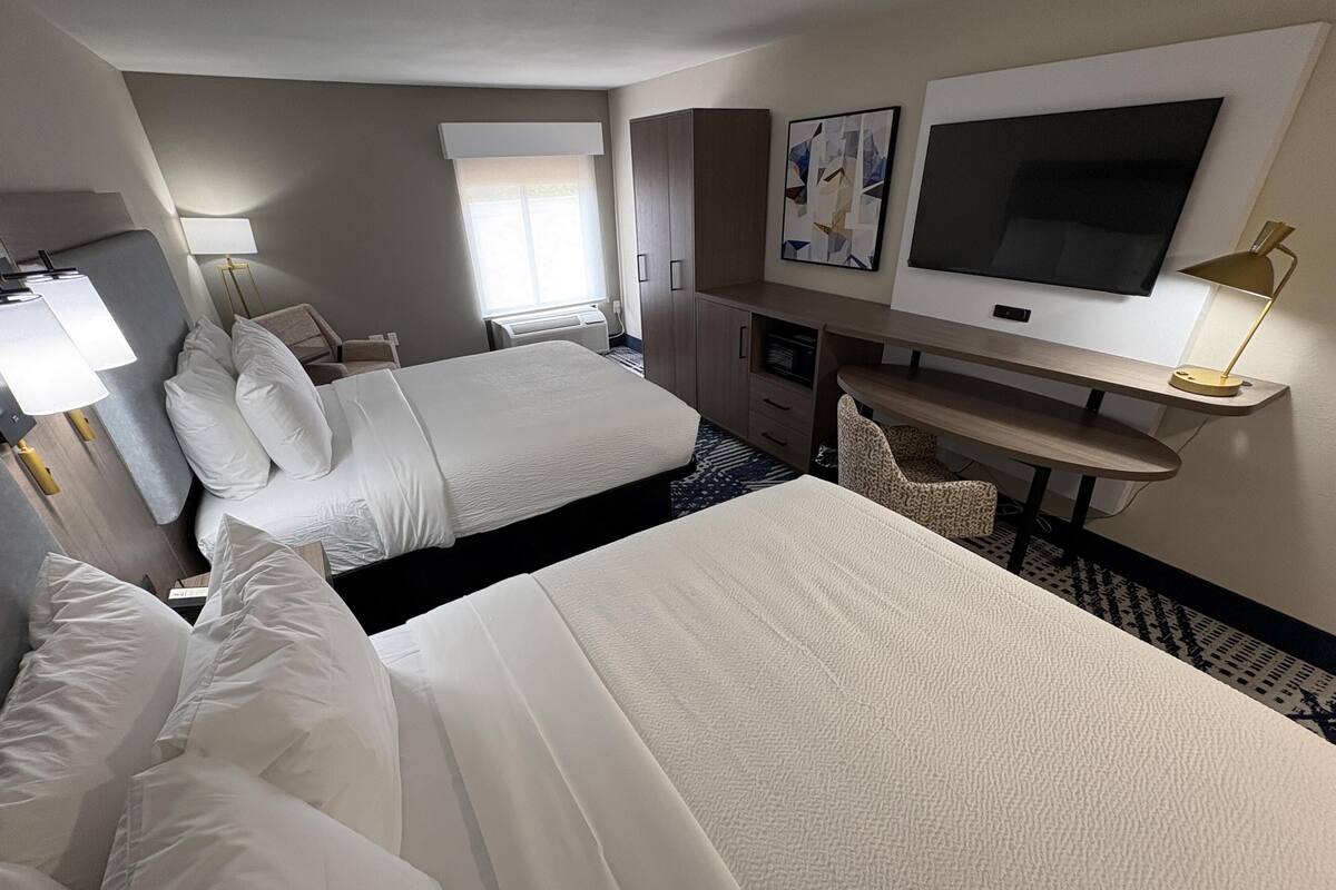 A hotel room with two beds, a desk, a television, and a chair.
