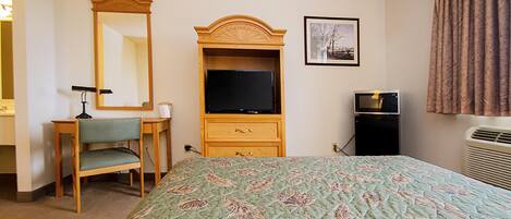 A hotel room with a bed, a desk, a television, a mirror, and an air conditioning unit.