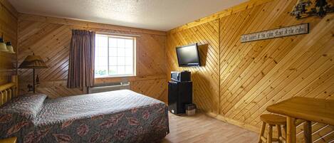 Een kamer in blokhutstijl met een bed, een televisie, een bureau en een raam.