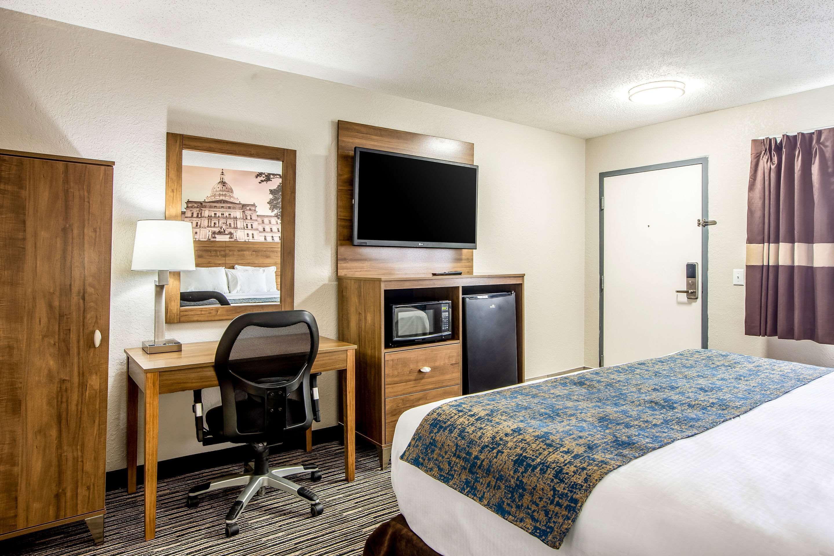 Une chambre d’hôtel équipée d’un lit, d’un bureau, d’une chaise, d’une télévision, d’un four à micro-ondes, d’un réfrigérateur et d’une porte.