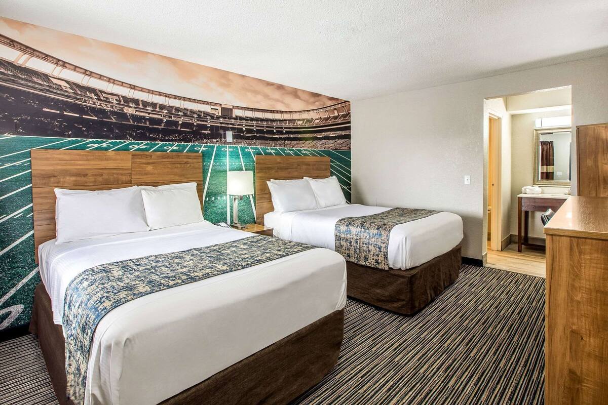 Une chambre d’hôtel avec deux lits, une grande fresque murale, une tête de lit en bois et un petit bureau avec un miroir.