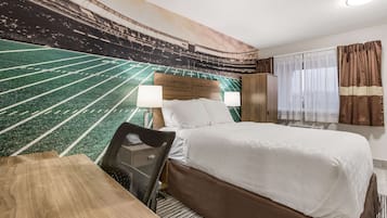 A hotel room with a bed, a desk, a chair, a large window with curtains, and a mural of a football field on the wall.