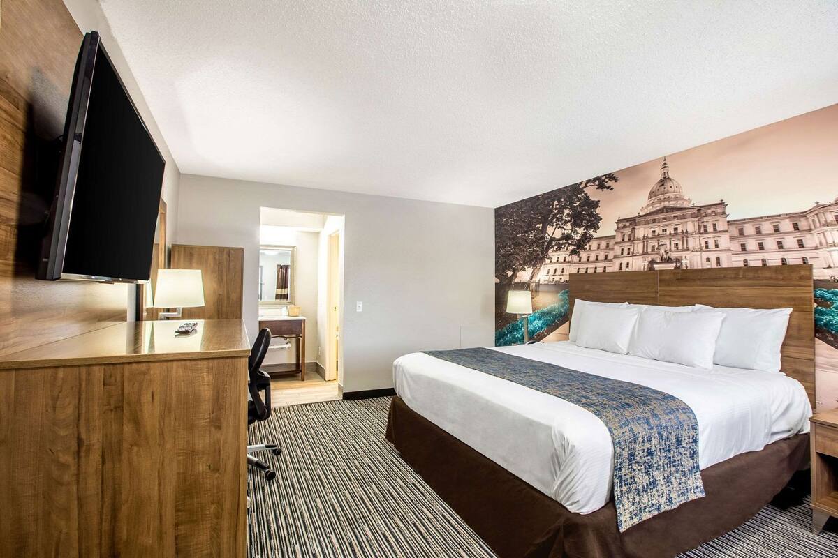Une chambre d’hôtel avec un lit, un bureau et une chaise, un téléviseur et une salle de bain visible à travers une porte ouverte.