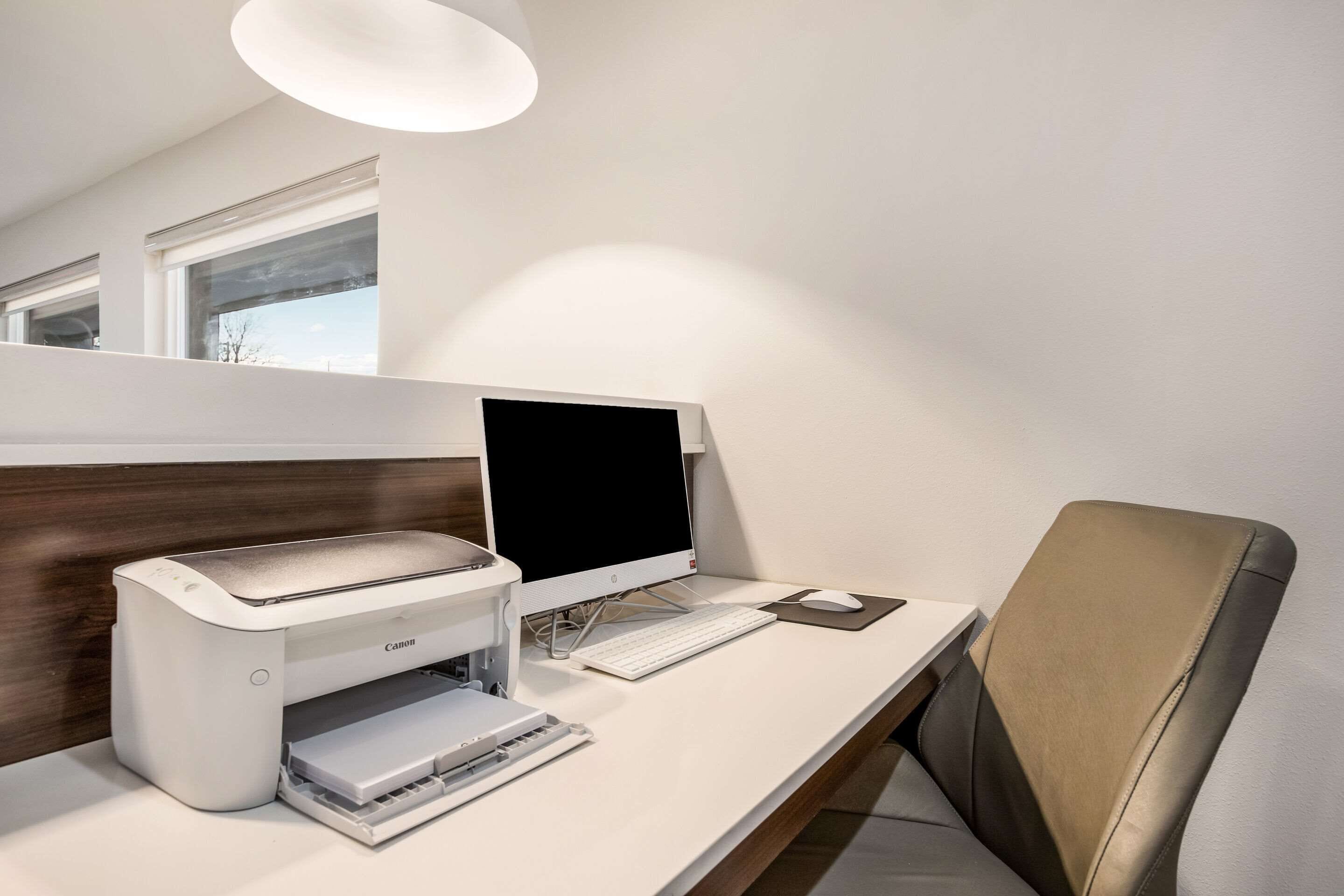 A modern office desk with a desktop computer, a printer, and a chair.