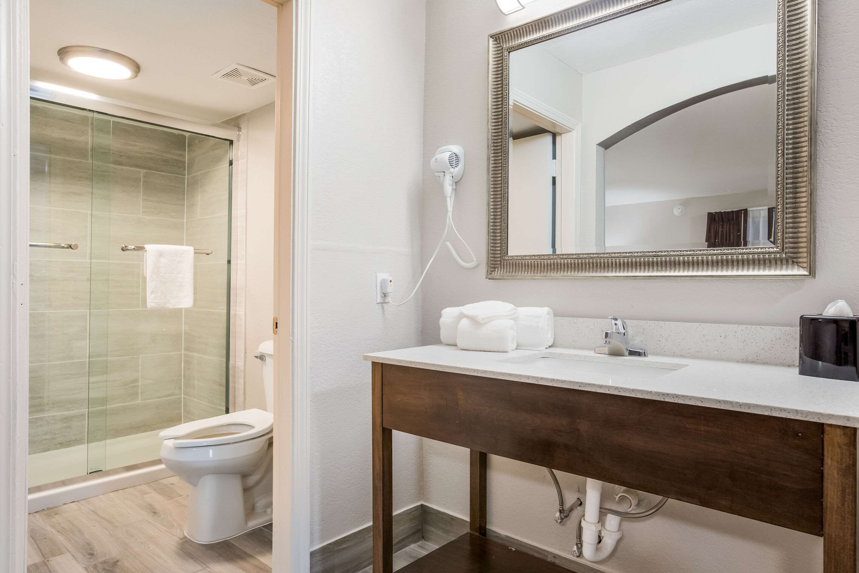 A bathroom with a glass shower enclosure, a white toilet, a wooden vanity with a mirror, and a towel rack.