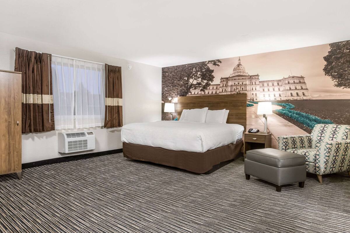 Une chambre d’hôtel avec un grand lit, un bureau avec une lampe, une chaise et un climatiseur fixé au mur.