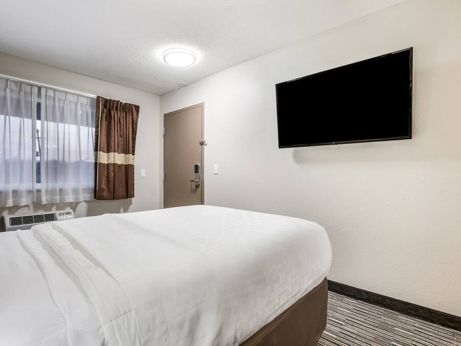 Quarto de hotel com uma cama, uma televisão de tela plana na parede, uma janela com cortinas e uma porta.
