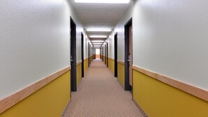 A long, narrow hallway with doors on both sides, carpeted floor, and fluorescent lighting. - Americas Best Value Inn Seymour (Seymour)