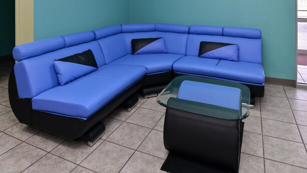 A blue sectional sofa with black cushions and a glass coffee table in a room with teal walls and tiled flooring. - Americas Best Value Inn Seymour (Seymour)