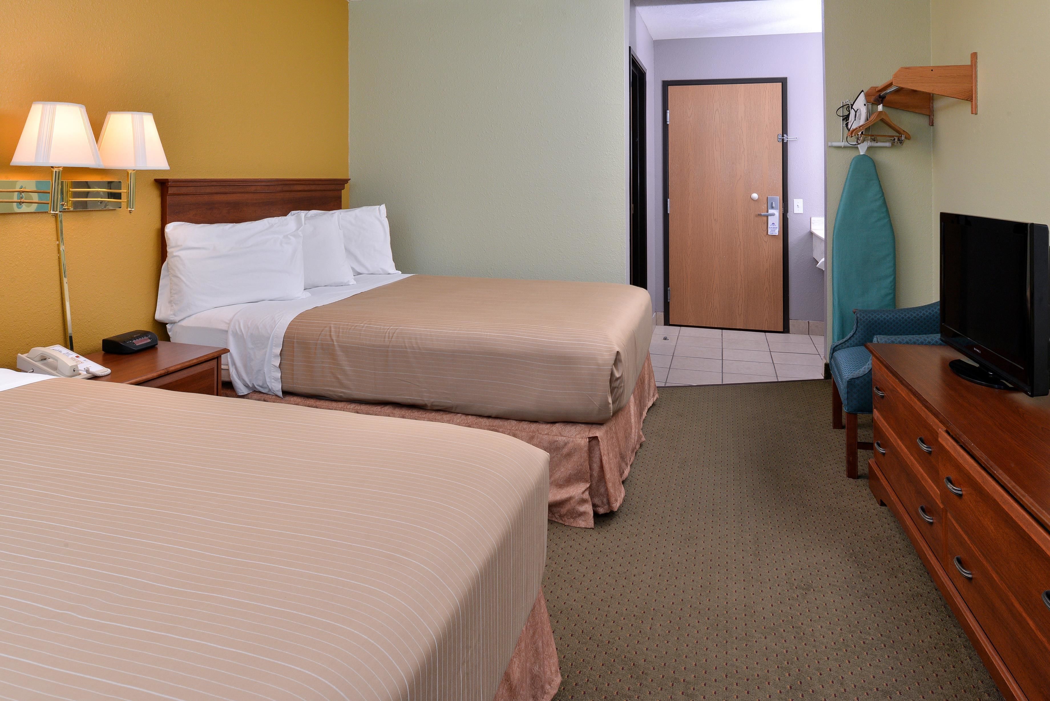 A hotel room with two beds, a desk with a telephone, a television, and a door leading to another room.