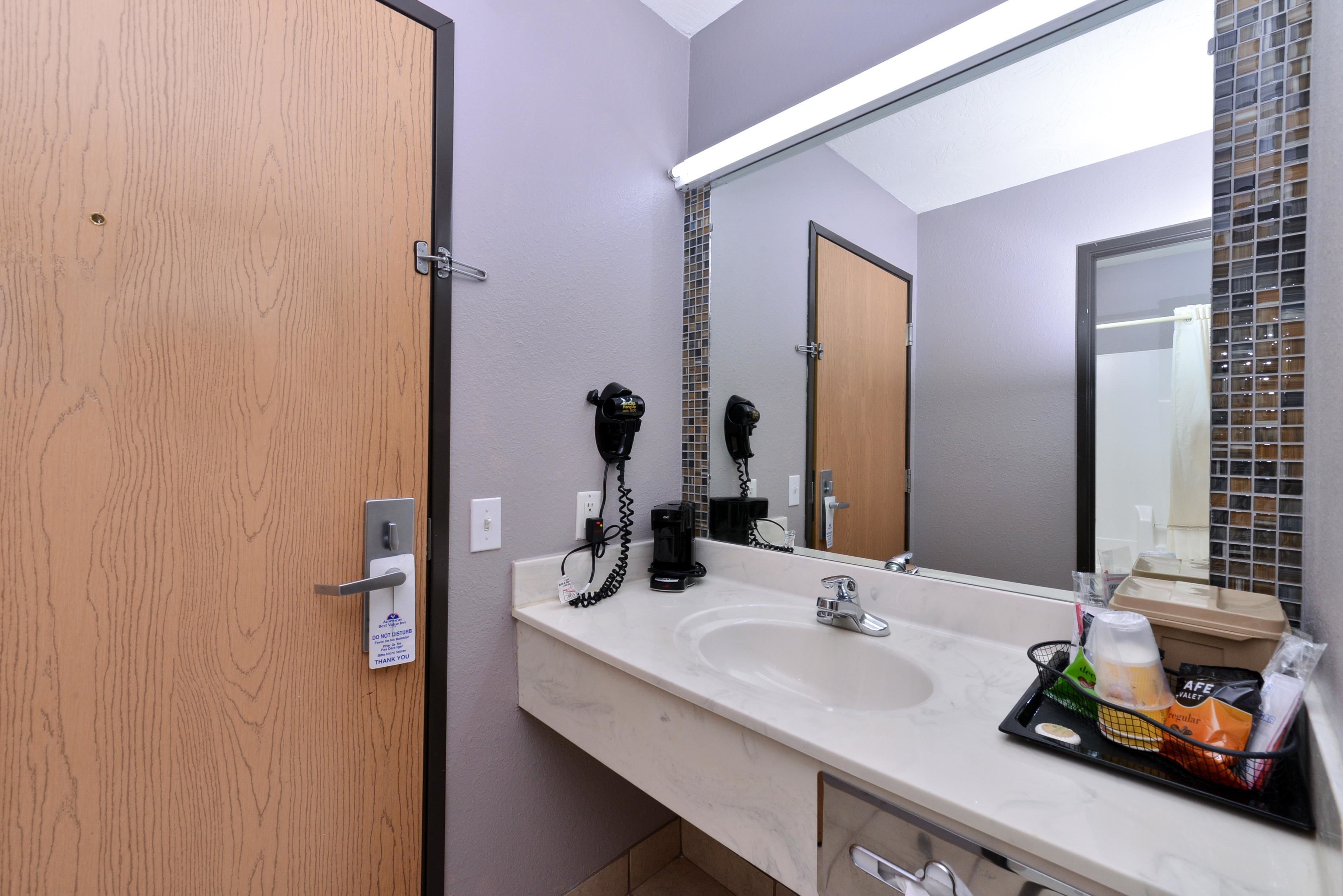 A hotel bathroom with a wooden door, a large mirror, a white sink, and a tray with toiletries.