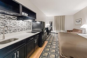 A compact hotel room with a kitchenette, a bed, a sofa, and a view of the city. - Suburban Studios Mason Hwy 42 (Mason)