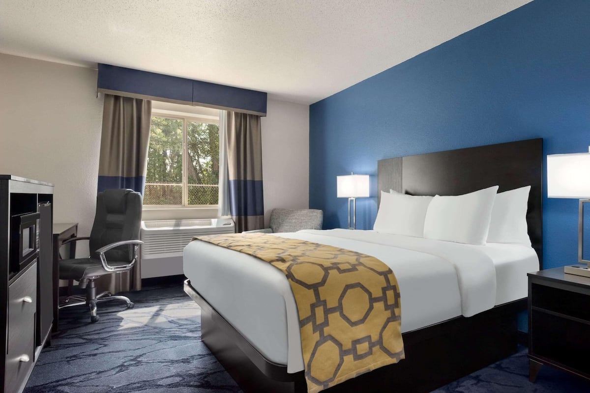 Una habitación de hotel con cama, escritorio, silla y ventana con cortinas.