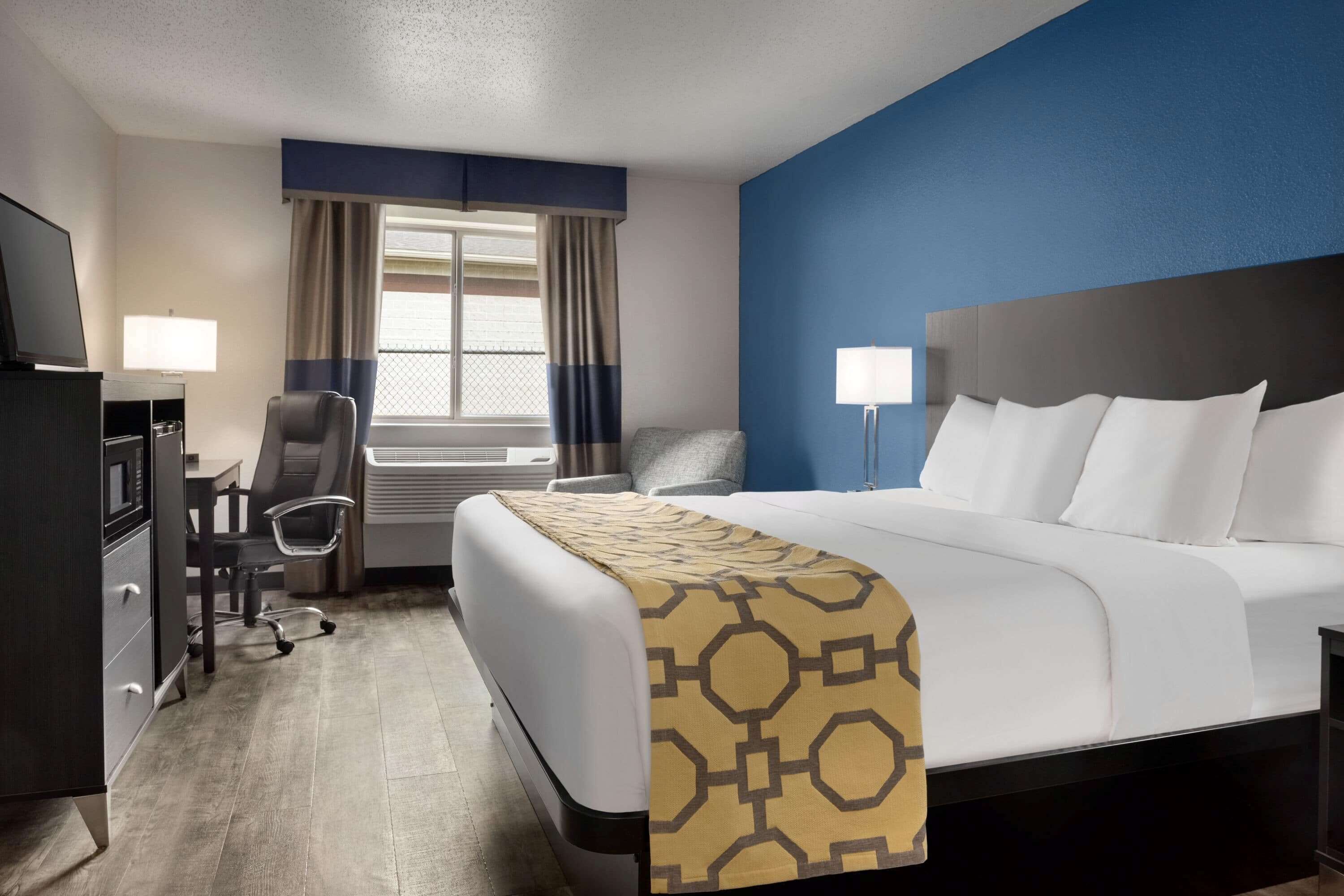 A hotel room with a bed, a desk, a chair, a TV, and a window with curtains.