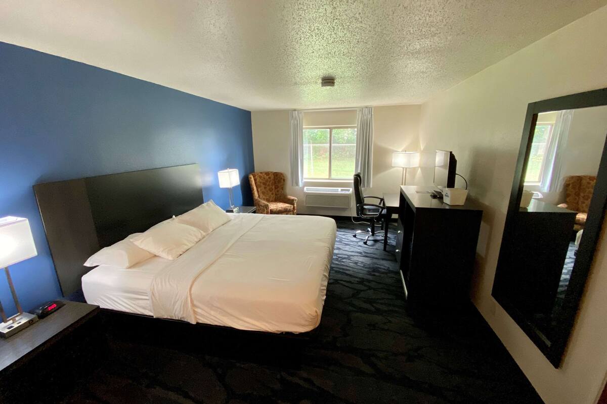 Una habitación de hotel con una cama grande, un escritorio, una silla, un espejo y una ventana con cortinas.