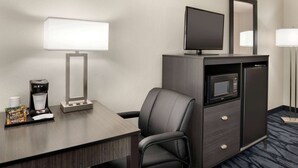 Une chambre d’hôtel équipée d’un bureau, d’une chaise, d’un four à micro-ondes, d’un réfrigérateur, d’une télévision et d’une lampe.