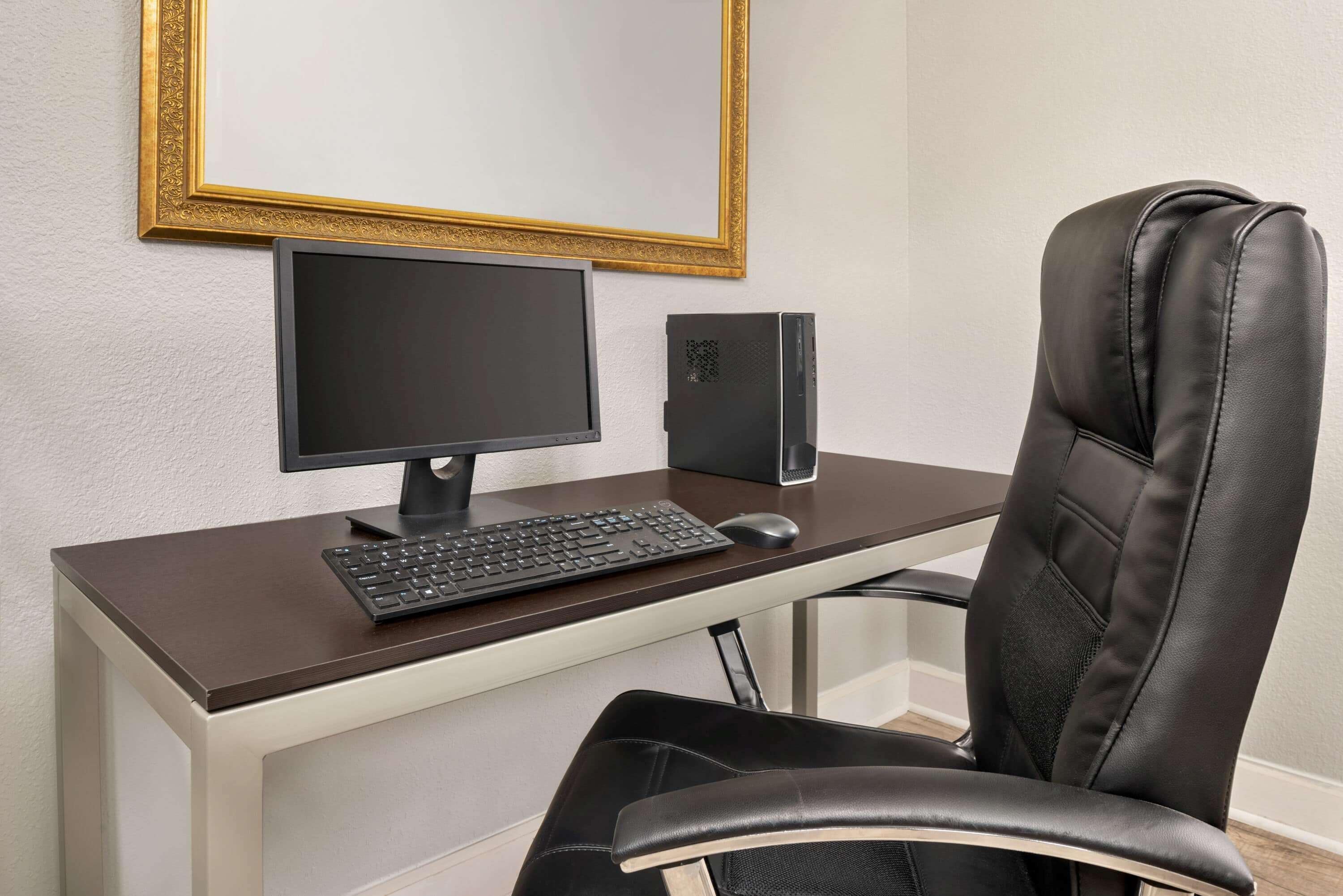 Un espacio de oficina moderno con escritorio, computadora, teclado, ratón y una silla de cuero.