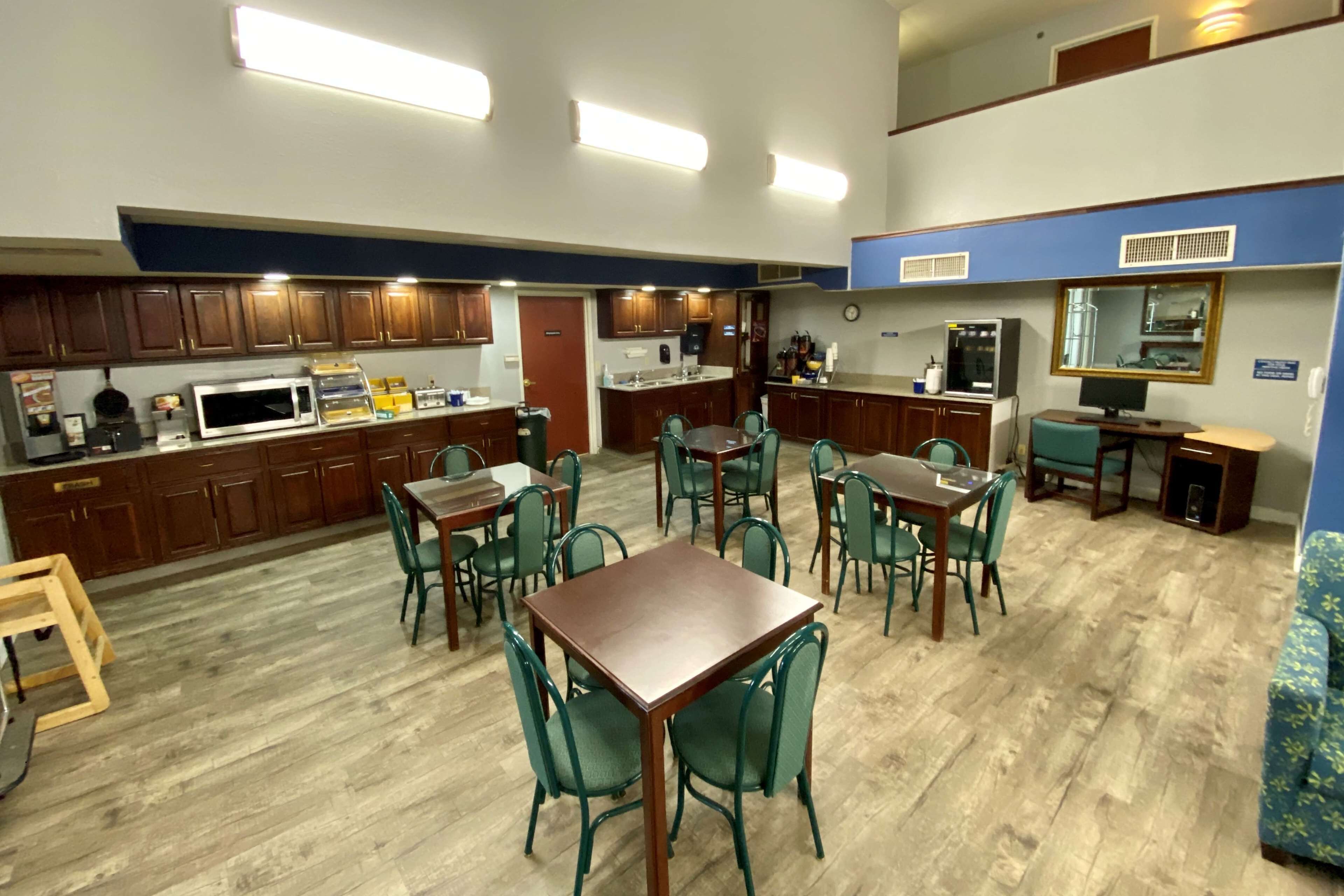 A dining area with wooden tables and chairs, a kitchen with wooden cabinets, and a microwave.
