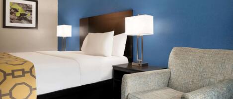 A hotel room with a bed, two bedside lamps, a chair, and a framed picture on the wall.