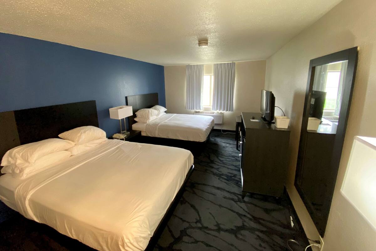 Habitación de hotel con dos camas, un escritorio, un espejo y un televisor.