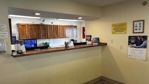 Un comptoir d’accueil avec des meubles de rangement en bois, un ordinateur et divers affiches d’information accrochées au mur.