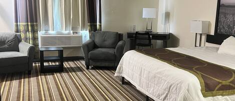 Una habitación de hotel con cama, sofá, sillón, escritorio y ventana con cortinas.