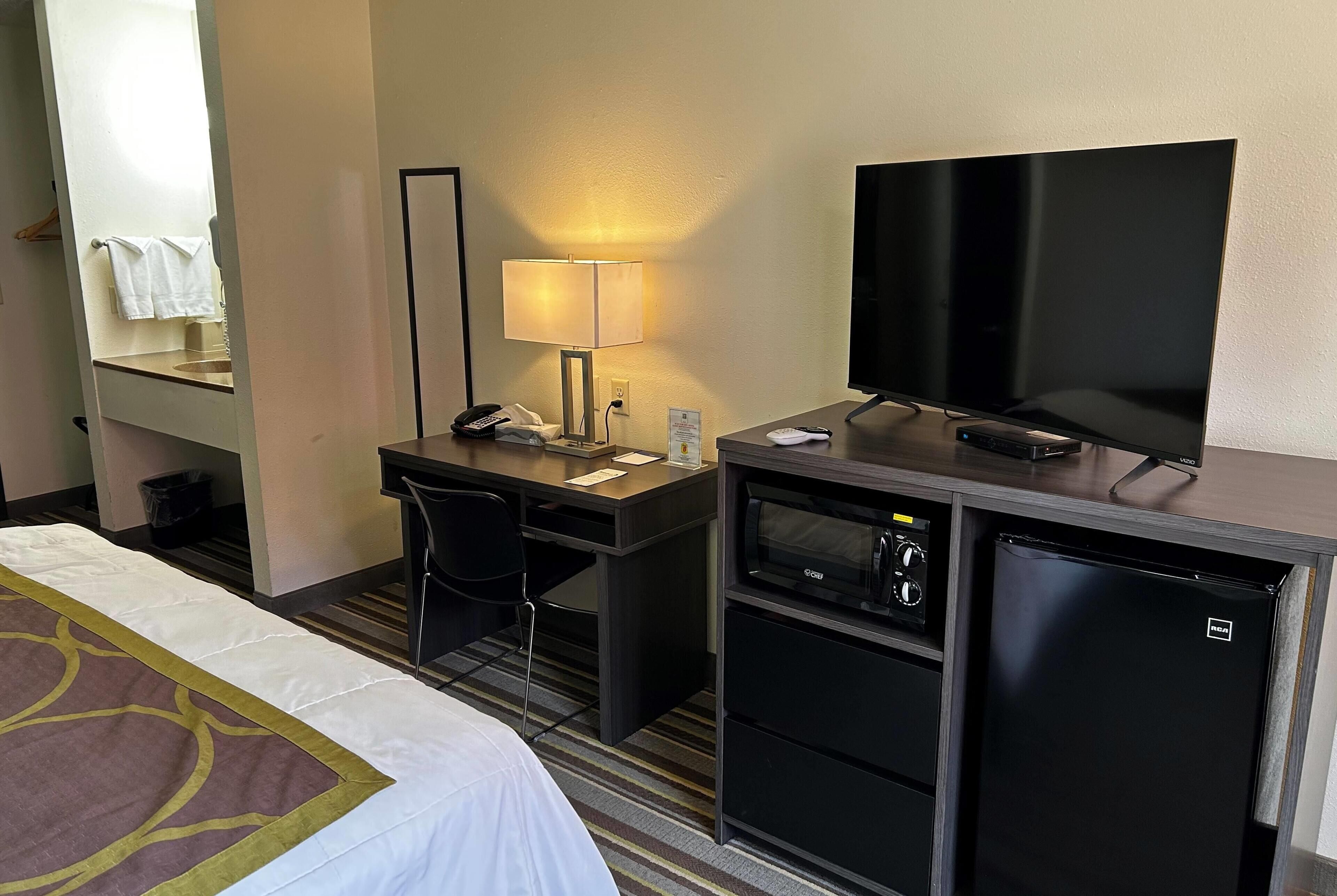 A hotel room with a bed, a desk with a lamp, a television, a mini-fridge, and a microwave.