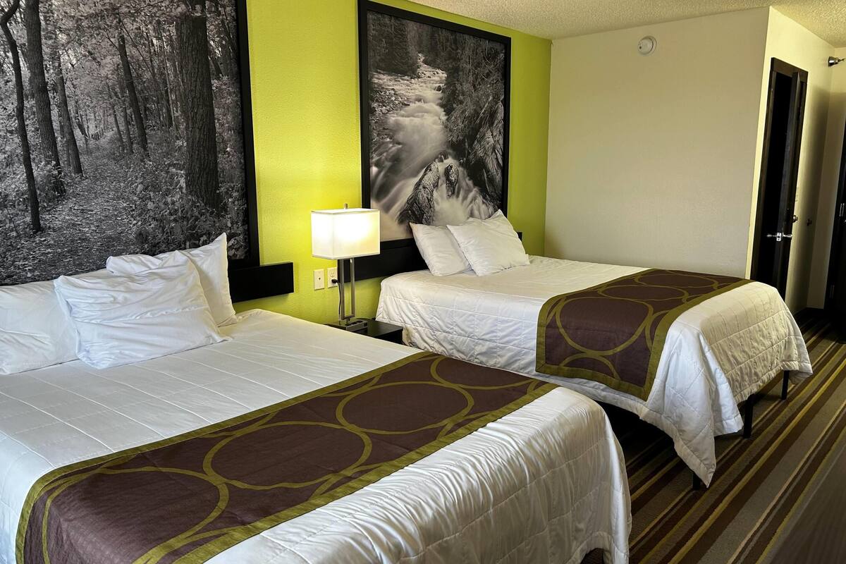 Una habitación de hotel con dos camas, un cuadro grande con tema de bosque en la pared y piso alfombrado.