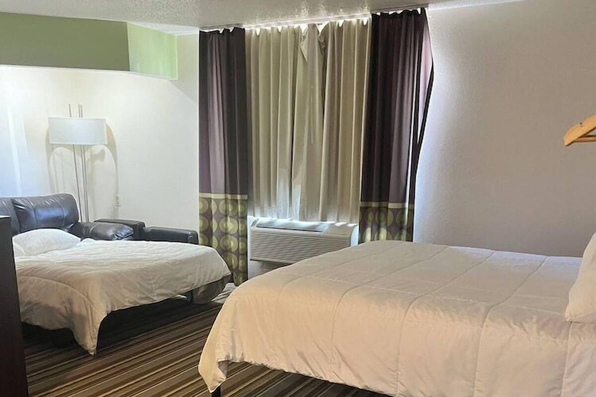 Habitación de hotel con una cama grande, una cama más pequeña, un escritorio, una silla y una ventana con cortinas.