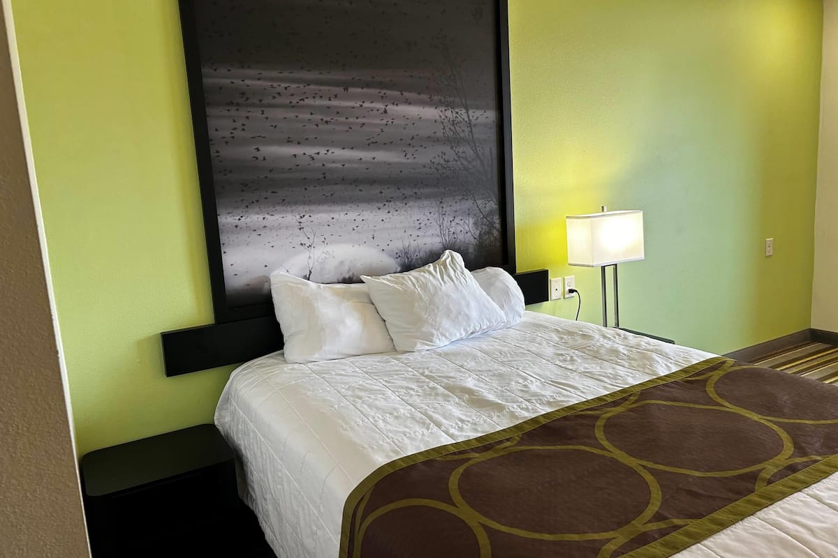 Habitación de hotel con cama, mesita de noche, lámpara y una gran obra de arte abstracta en la pared.