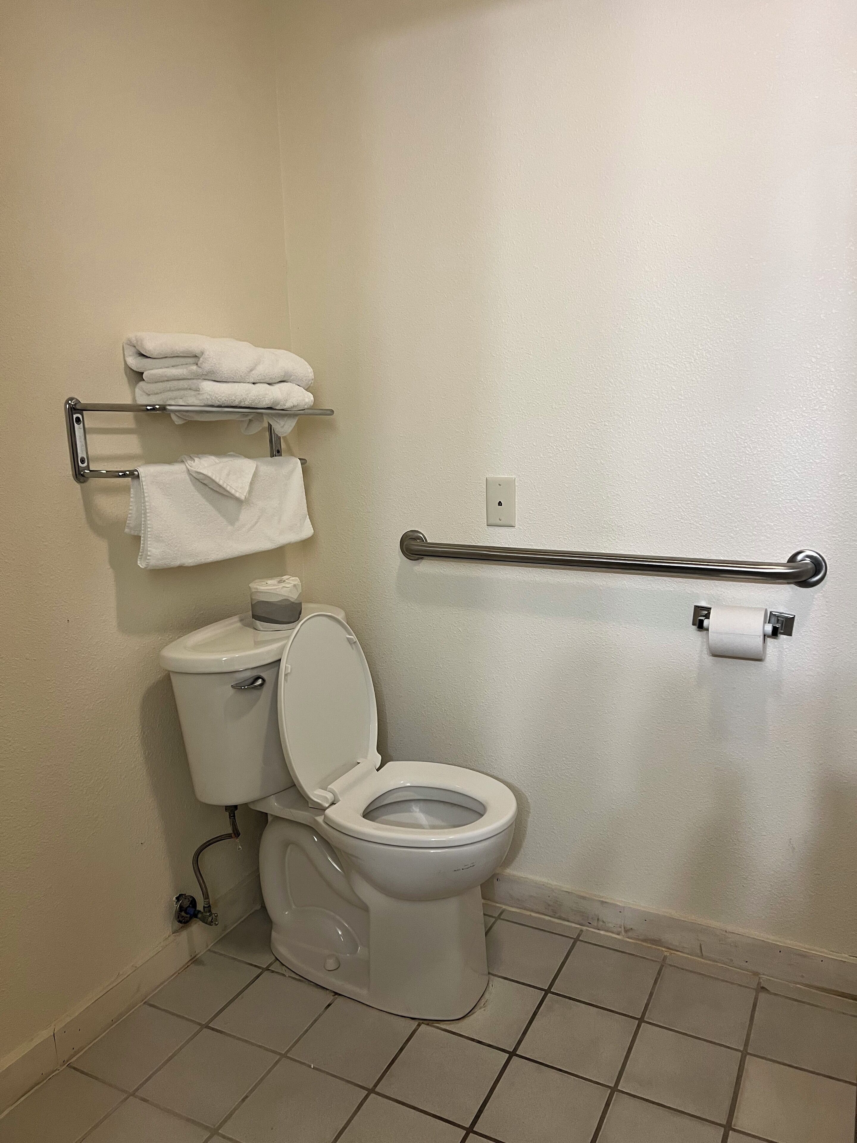 Une salle de bain équipée de toilettes, d’un porte-serviettes avec des serviettes pliées et d’une barre d’appui.