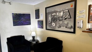 Une pièce comprenant deux fauteuils noirs, une petite table avec une lampe et un tableau encadré représentant un bâtiment.