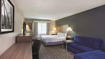 Una habitación de hotel con una cama, un escritorio, un sofá azul y un ventanal con cortinas.