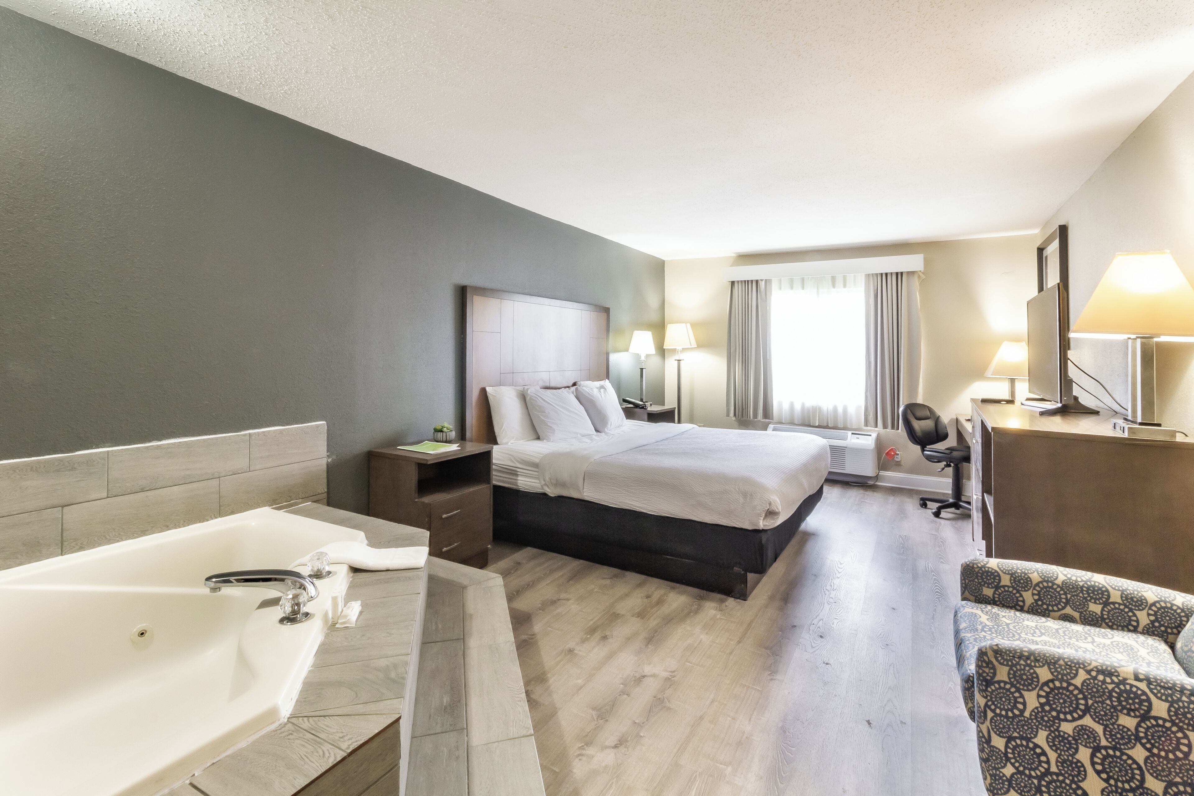 Een hotelkamer met een groot bed, een apart bureau, een stoel, een bureaulamp, een televisie en een badkamer met bad en wastafel.