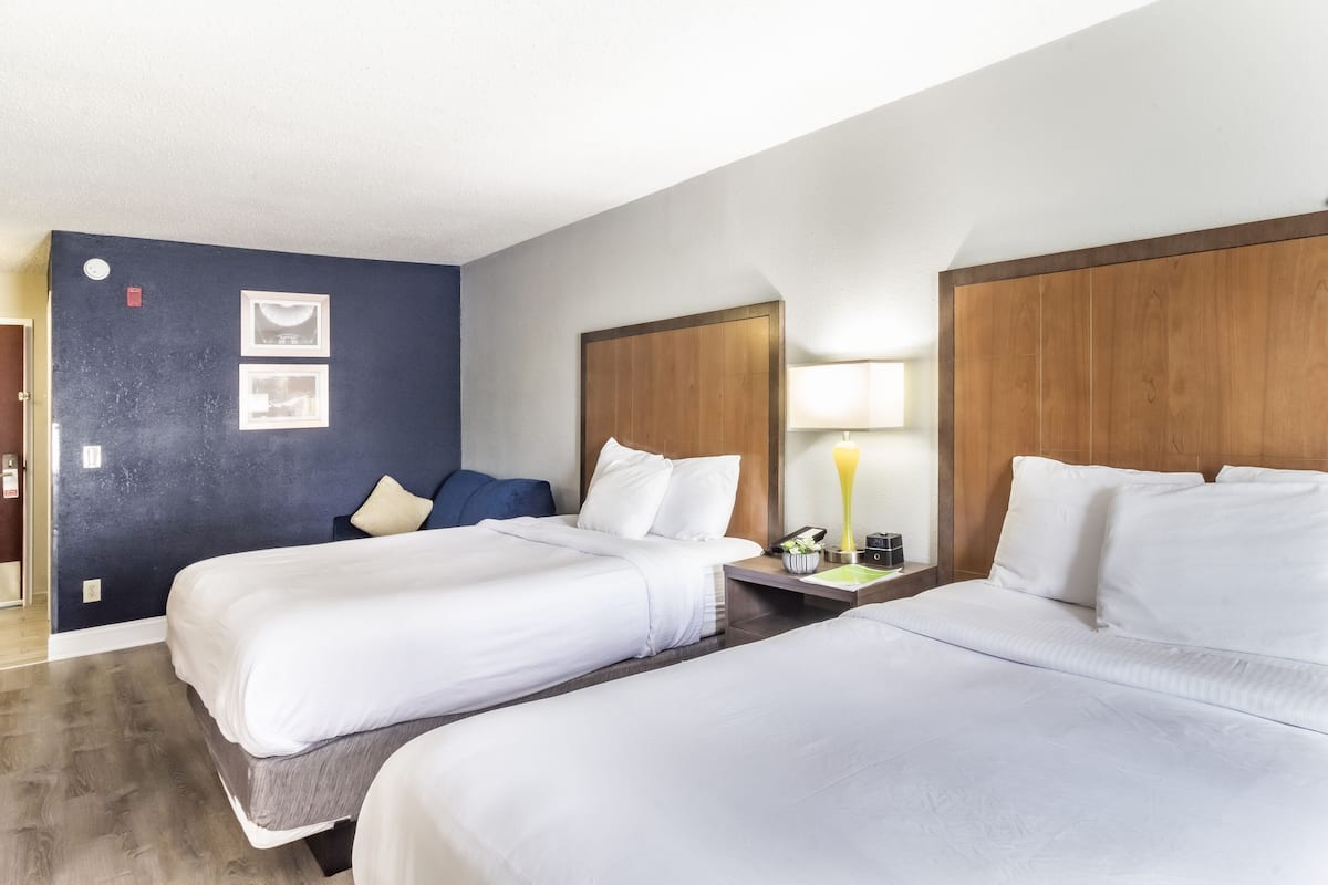 Een hotelkamer met twee bedden, een houten hoofdbord, een nachtkastje met een lamp en een aan de muur bevestigde telefoon.