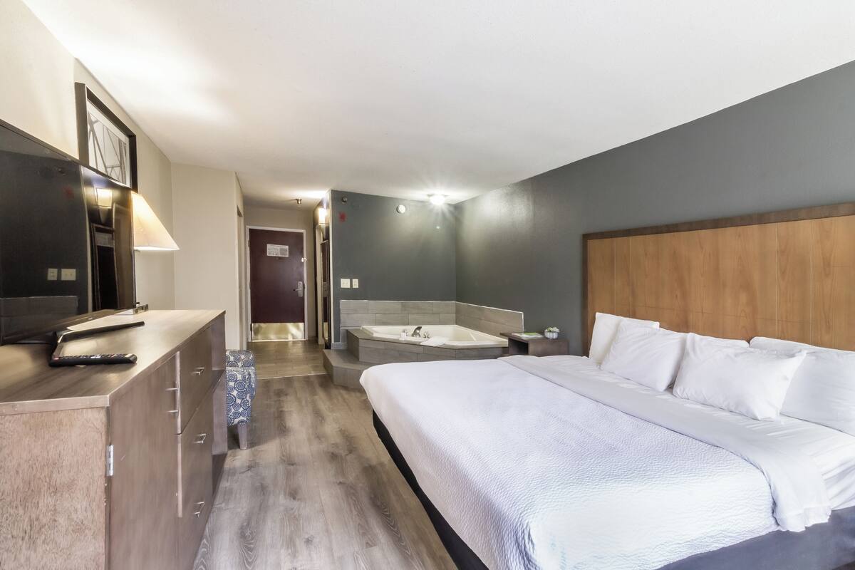 Een hotelkamer met een bed, een bureau met lamp, een badkuip en een kleine plant.