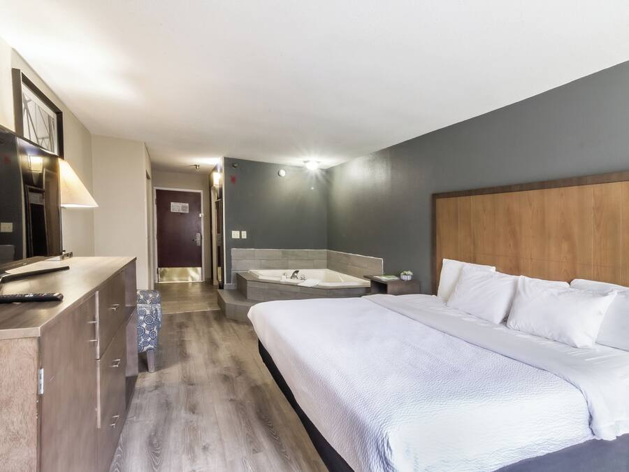Quarto de hotel com cama, escrivaninha com luminária, banheira e uma pequena planta.