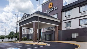Entrada de un hotel con estacionamiento techado, cielo despejado y un letrero que dice "LA QUINTA".