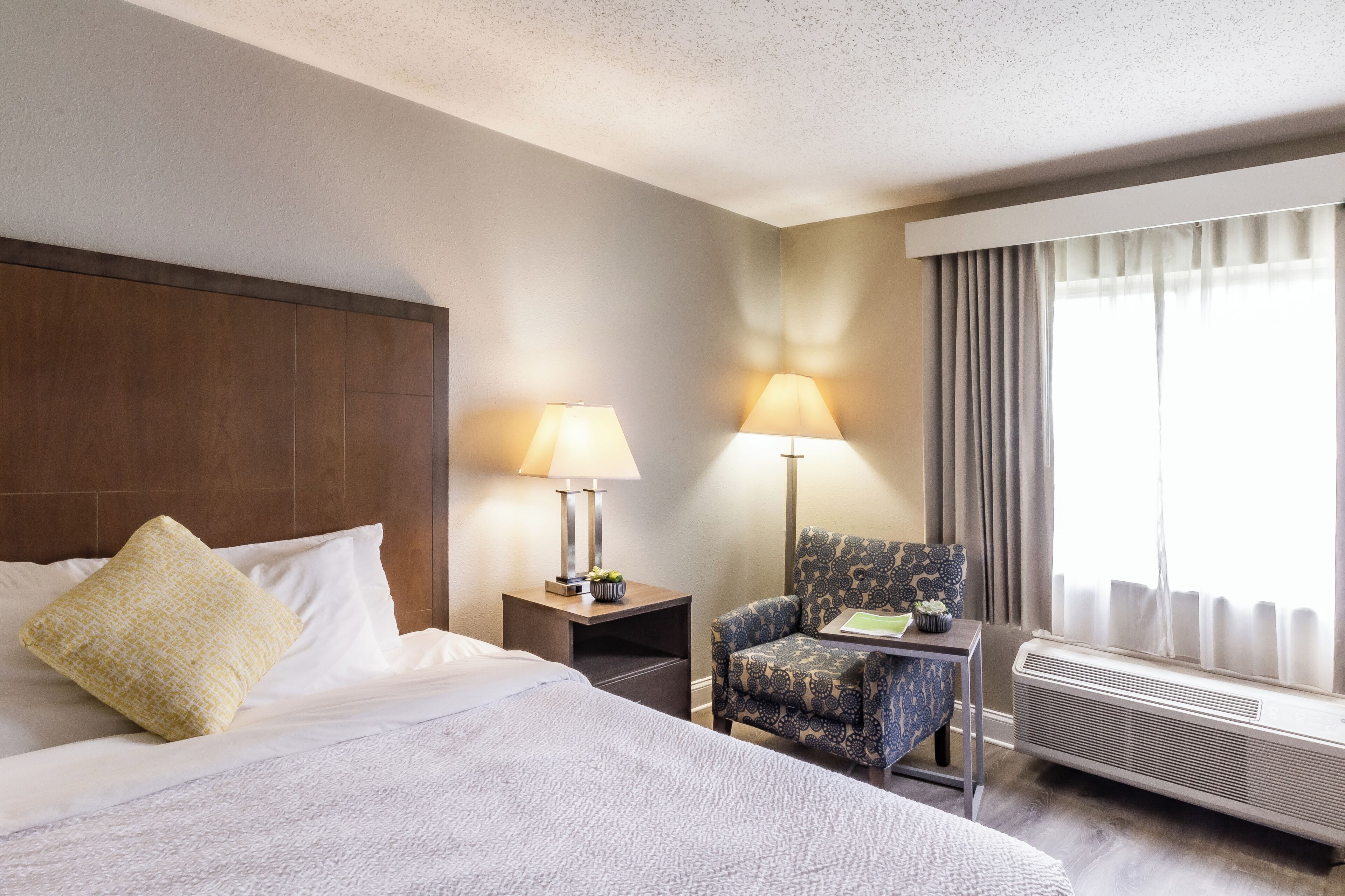 Une chambre d’hôtel avec un grand lit, deux tables de chevet avec des lampes, une chaise et un appareil de climatisation.