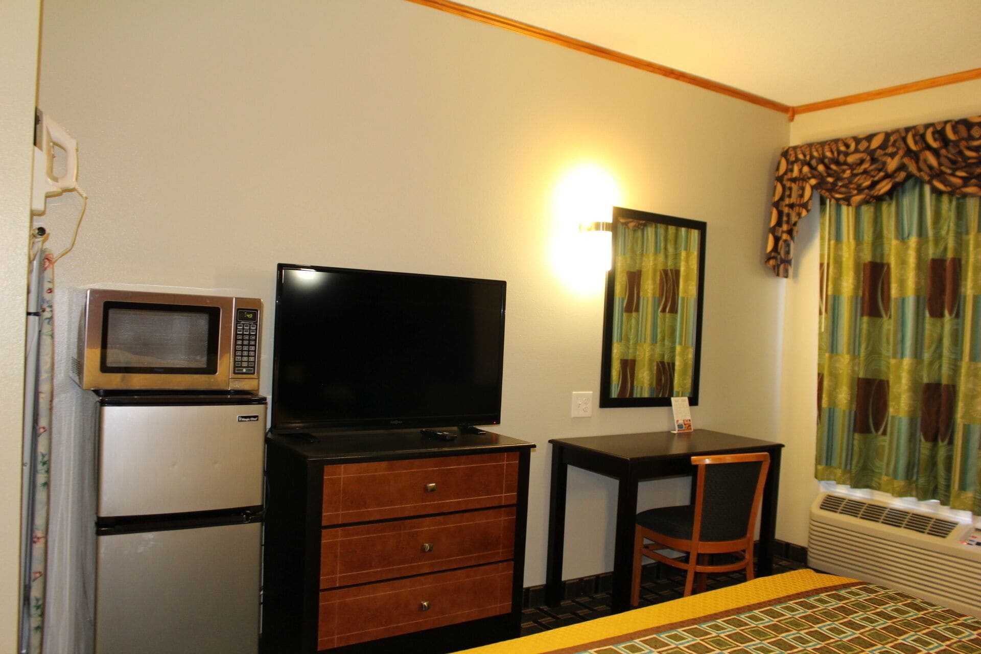 Habitación de hotel con televisión, microondas, escritorio, silla y ventana con cortinas.