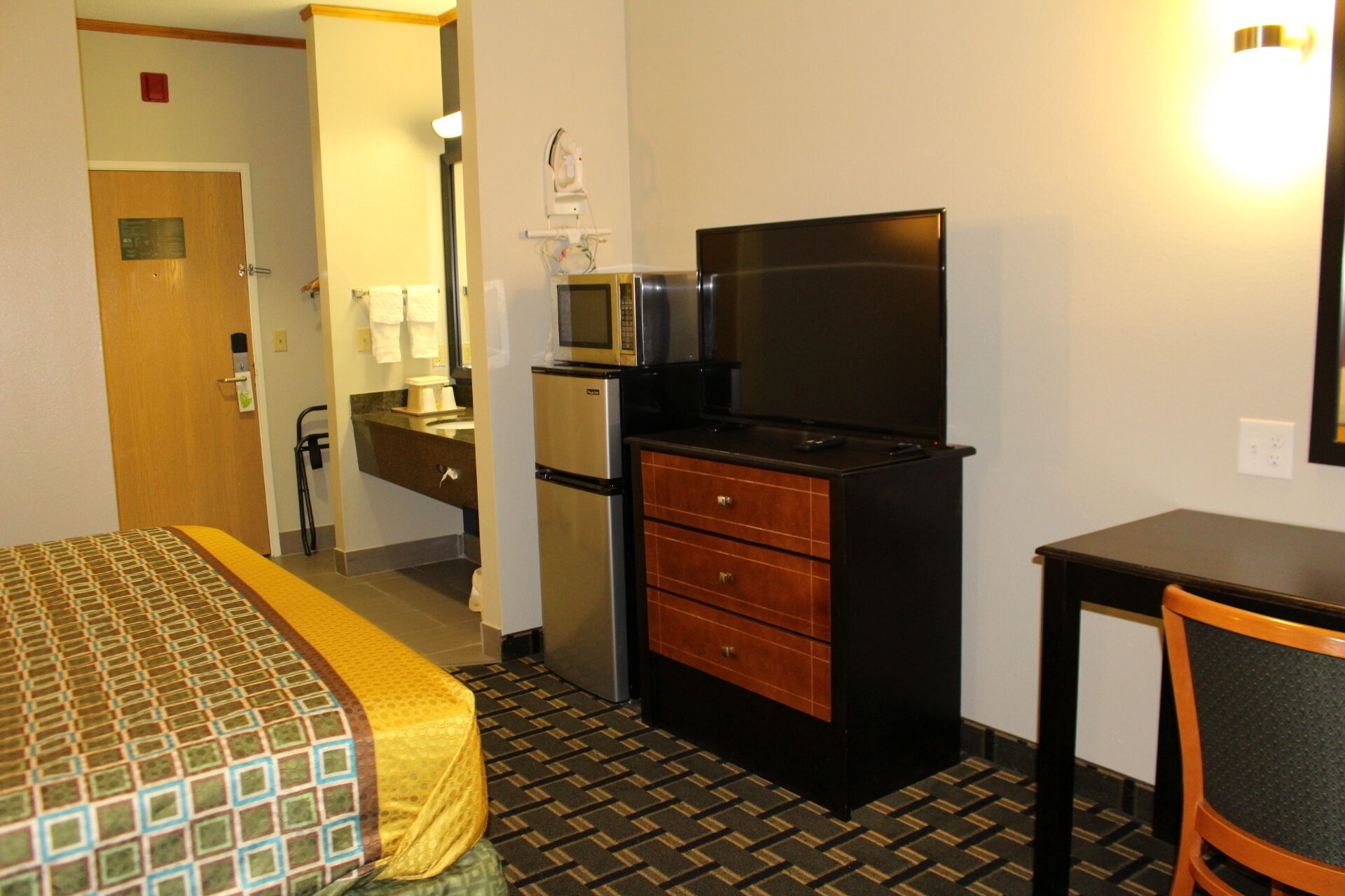 Habitación de hotel con cama, escritorio, televisión, refrigerador y microondas.